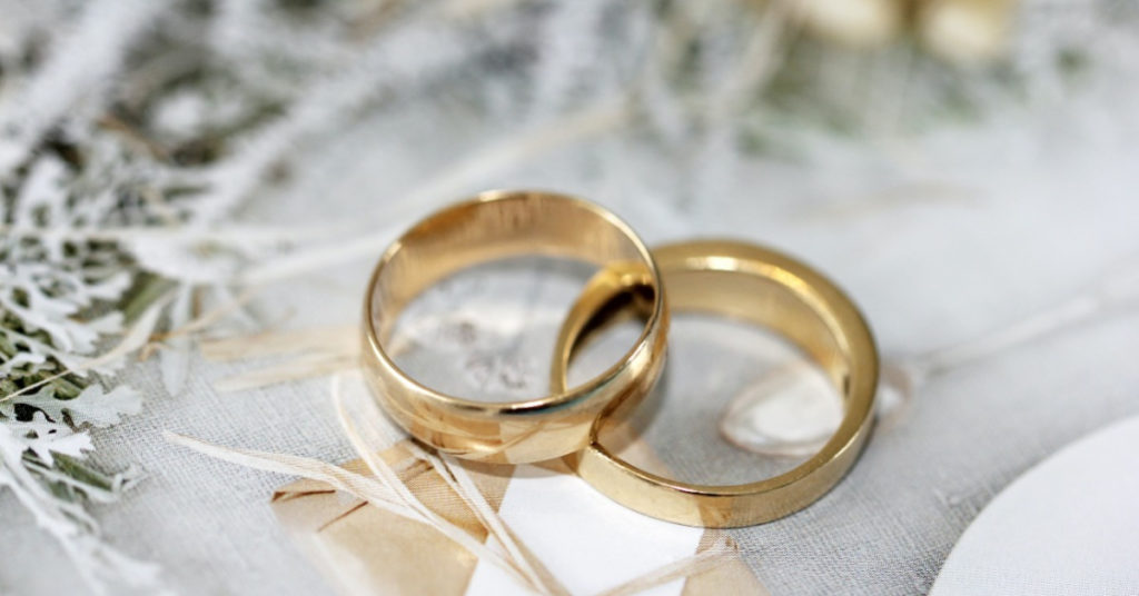 Two gold wedding rings on a fancy tablecloth show the theme of a wedding and a rabbi.